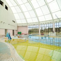 Una piscina interior con techo de vidrio, varias pistas de natación y un tobogán.