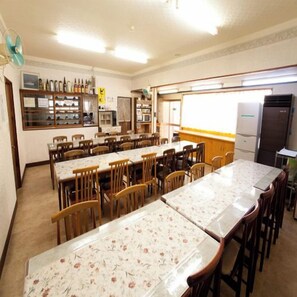 Un comedor con varias mesas y sillas, un refrigerador y una ventana con persianas.