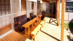 Een houten terras buiten met een overdekte zithoek, met banken en stoelen.