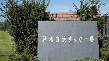 Placa de pedra com caracteres japoneses, rodeada por vegetação e uma cerca.