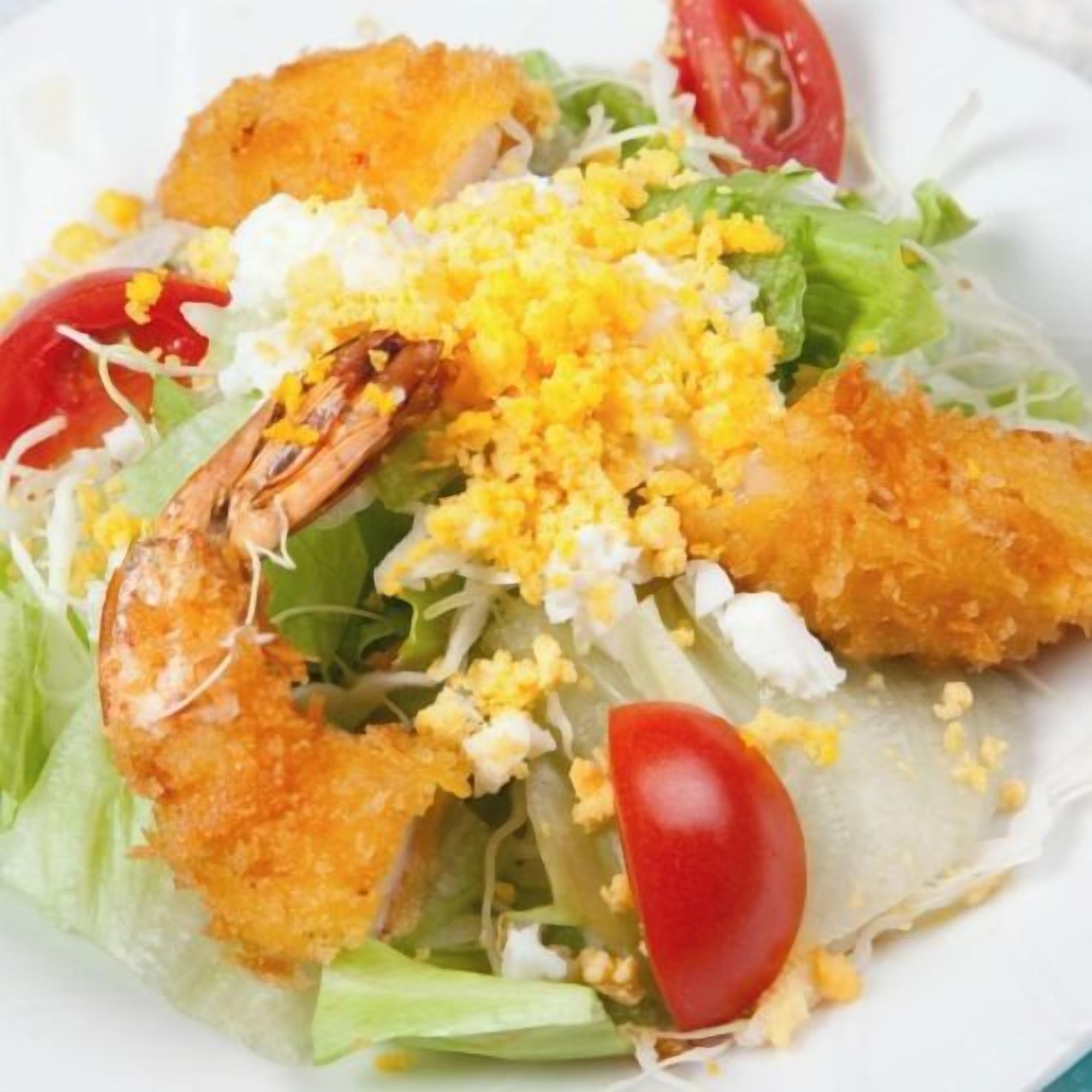 A salad with various ingredients including lettuce, cherry tomatoes, and a breaded item.