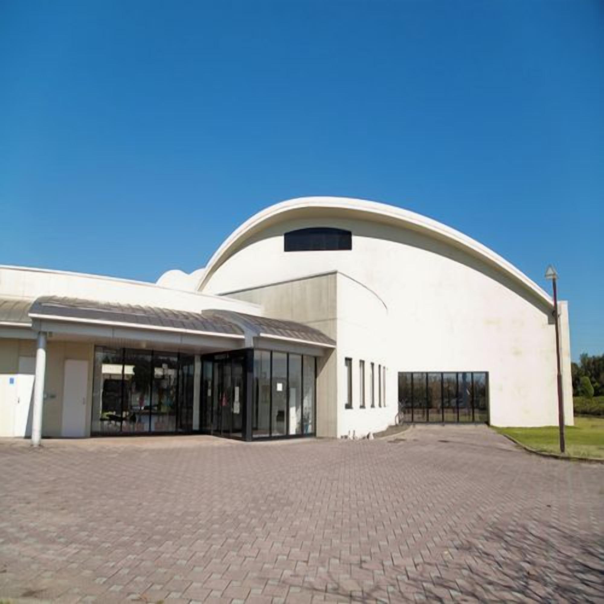 Um edifício moderno com telhado curvo e área de entrada coberta.
