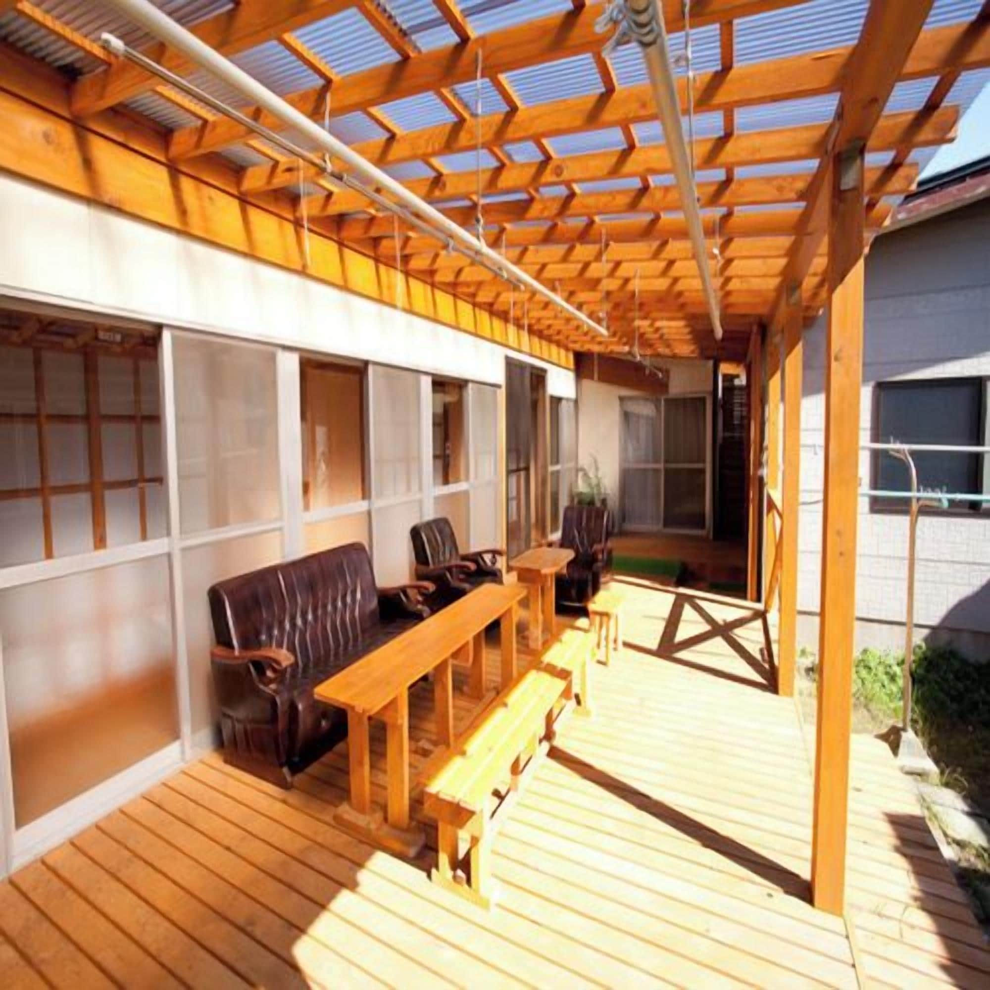 Een houten terras buiten met een bank, stoelen, een tafel en een pergola.