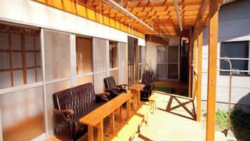Een houten terras buiten met een bank, stoelen, een tafel en een pergola.
