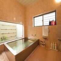 Un baño con una bañera grande, una ventana y un estante con artículos de aseo.