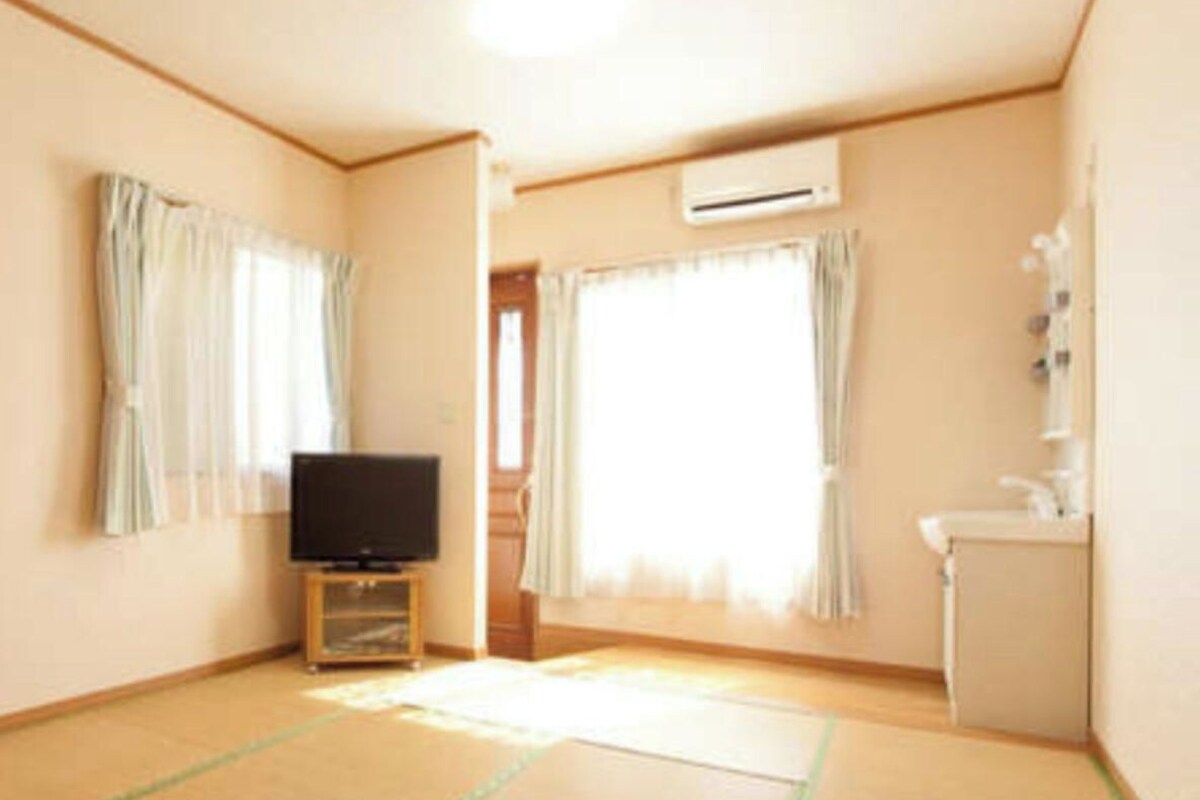Habitación con televisión sobre un mueble, lavamanos y ventana con cortinas.