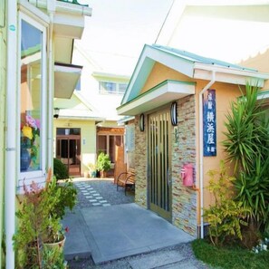 A building with a gated entrance, a small garden area with potted plants, and a signboard.