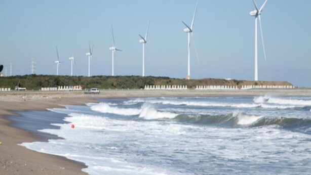 Een strand met golven en windturbines op de achtergrond.