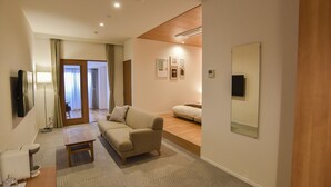 Ein modernes Hotelzimmer mit Sofa, Flachbildfernseher, Nachttisch und großem Spiegel.