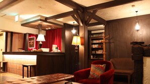 Ein gemütliches Zimmer mit Holzboden, einem roten Sessel, einer Ledbank und einem Bücherregal.