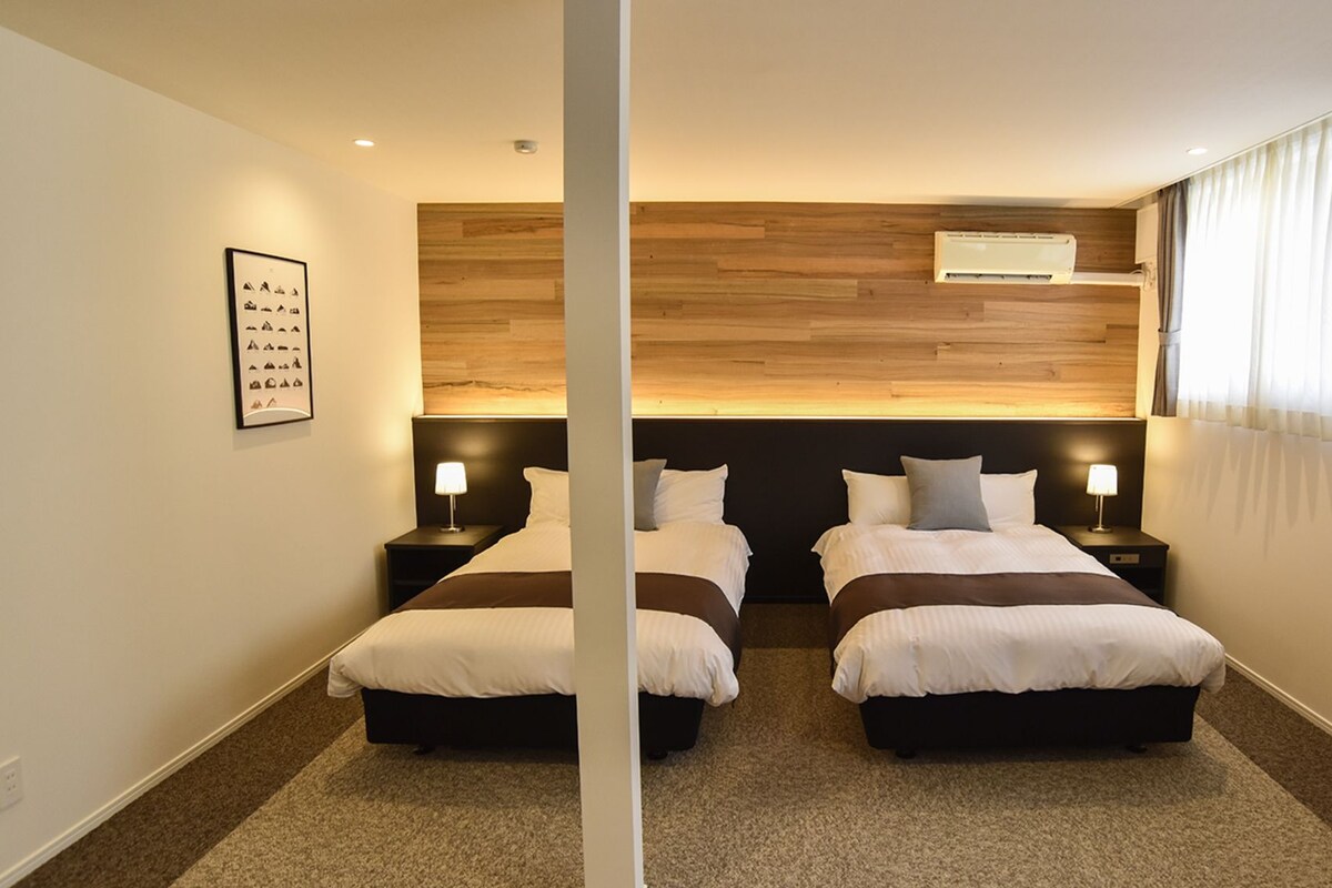 A hotel room with two beds, a wooden headboard, an air conditioning unit, and a framed picture on the wall.