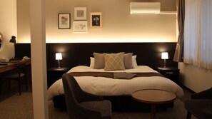 Una habitación de hotel con cama, dos mesitas de noche, un escritorio, una silla y una pequeña mesa redonda. Hay tres cuadros enmarcados en la pared sobre la cama.