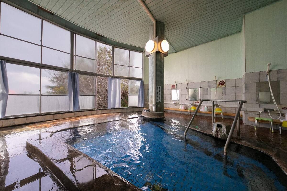 Une piscine intérieure dotée de grandes baies vitrées, d’un pilier central et d’un espace vestiaire avec des bancs et un miroir.