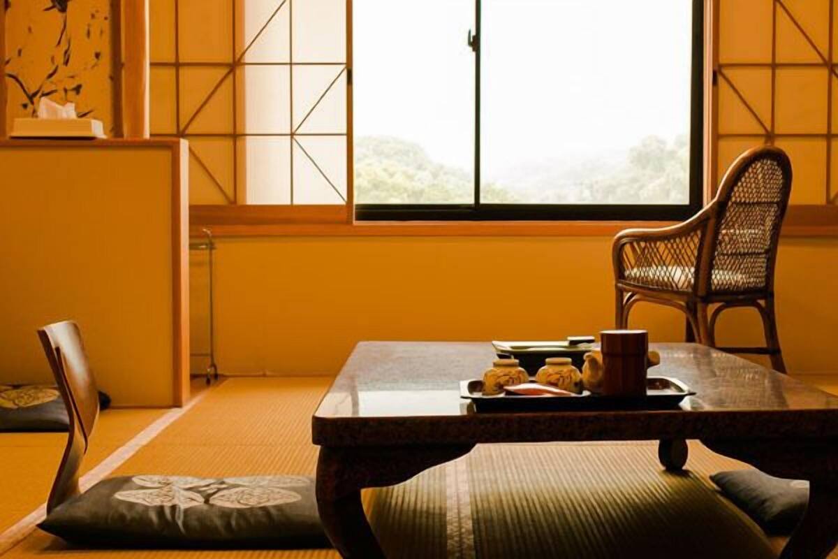 Une pièce de style japonais traditionnel, avec un sol recouvert de tatamis, une petite table sur laquelle est posé un plateau de nourriture, une chaise en osier et une vue à travers un paravent en papier.