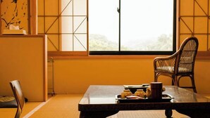 Une pièce de style japonais traditionnel, avec un sol recouvert de tatamis, une petite table sur laquelle est posé un plateau de collations, une chaise en bois et une vue sur le paysage à travers un paravent shoji.