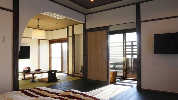 A spacious bedroom with a large bed, a television, and a view through a sliding door to a balcony. - Uehisa (Toba)