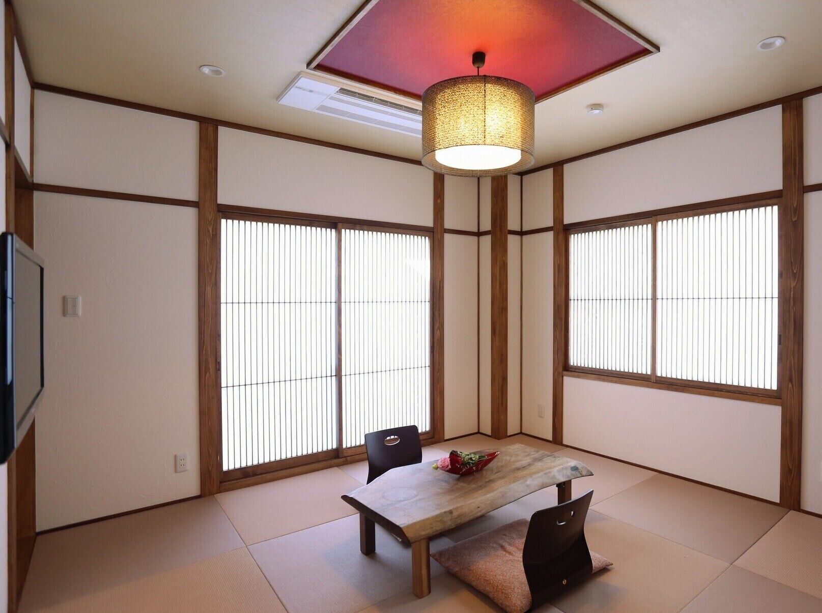 A traditional Japanese-style room with tatami flooring, shoji screens, a low table with chairs, and a hanging light fixture.