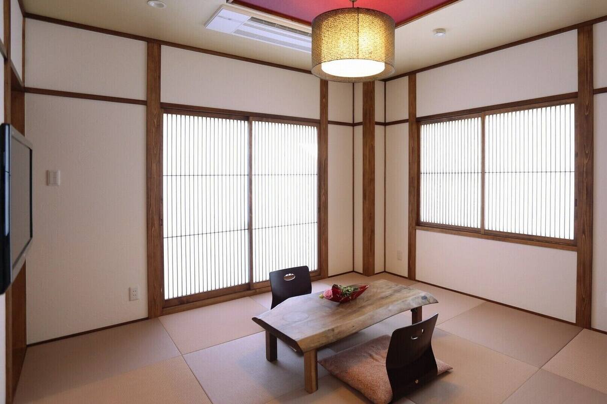 A traditional Japanese-style room with tatami flooring, shoji screens, a low table with chairs, and a hanging light fixture.