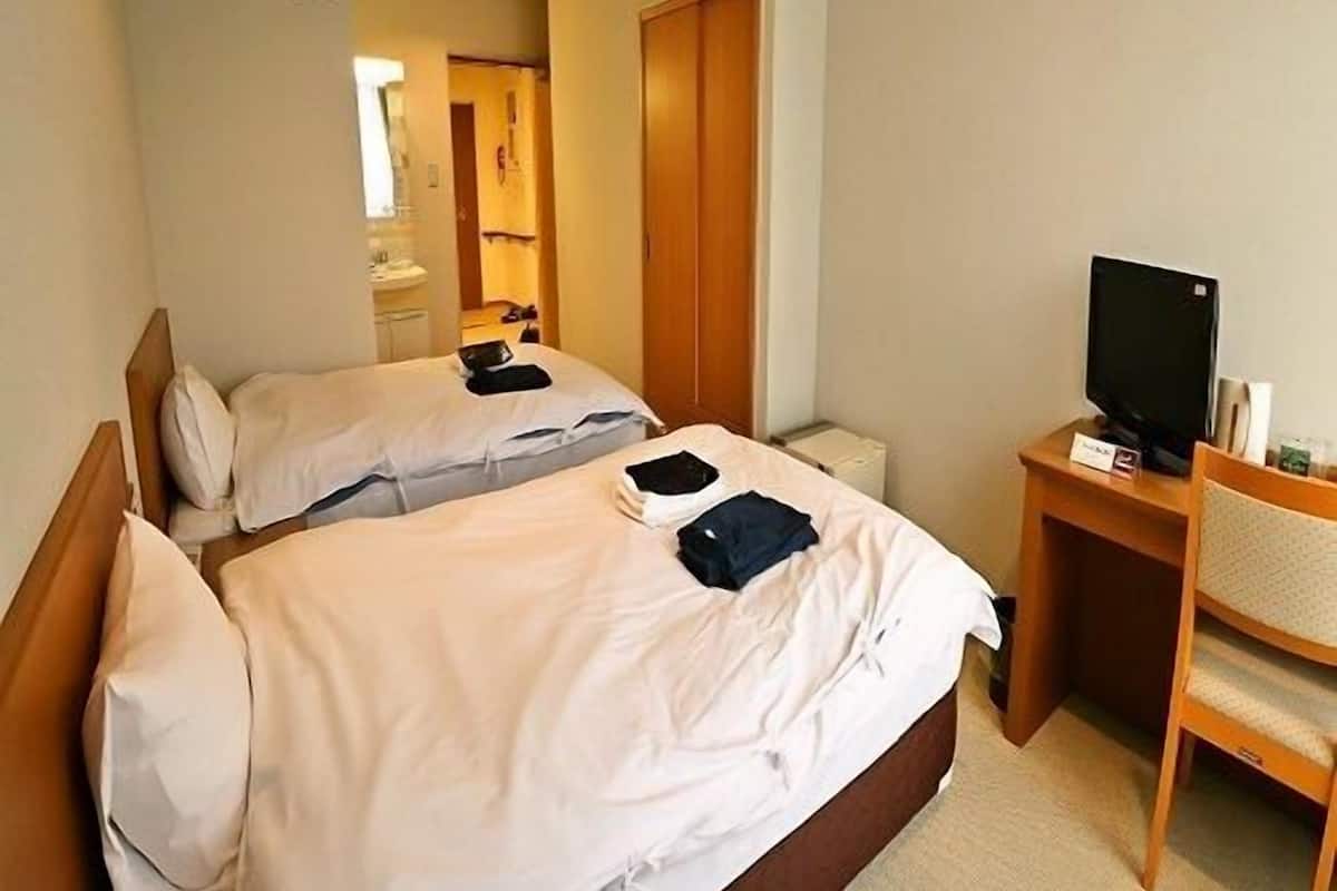 Une chambre d’hôtel avec deux lits, un bureau avec une télévision et une horloge au mur.