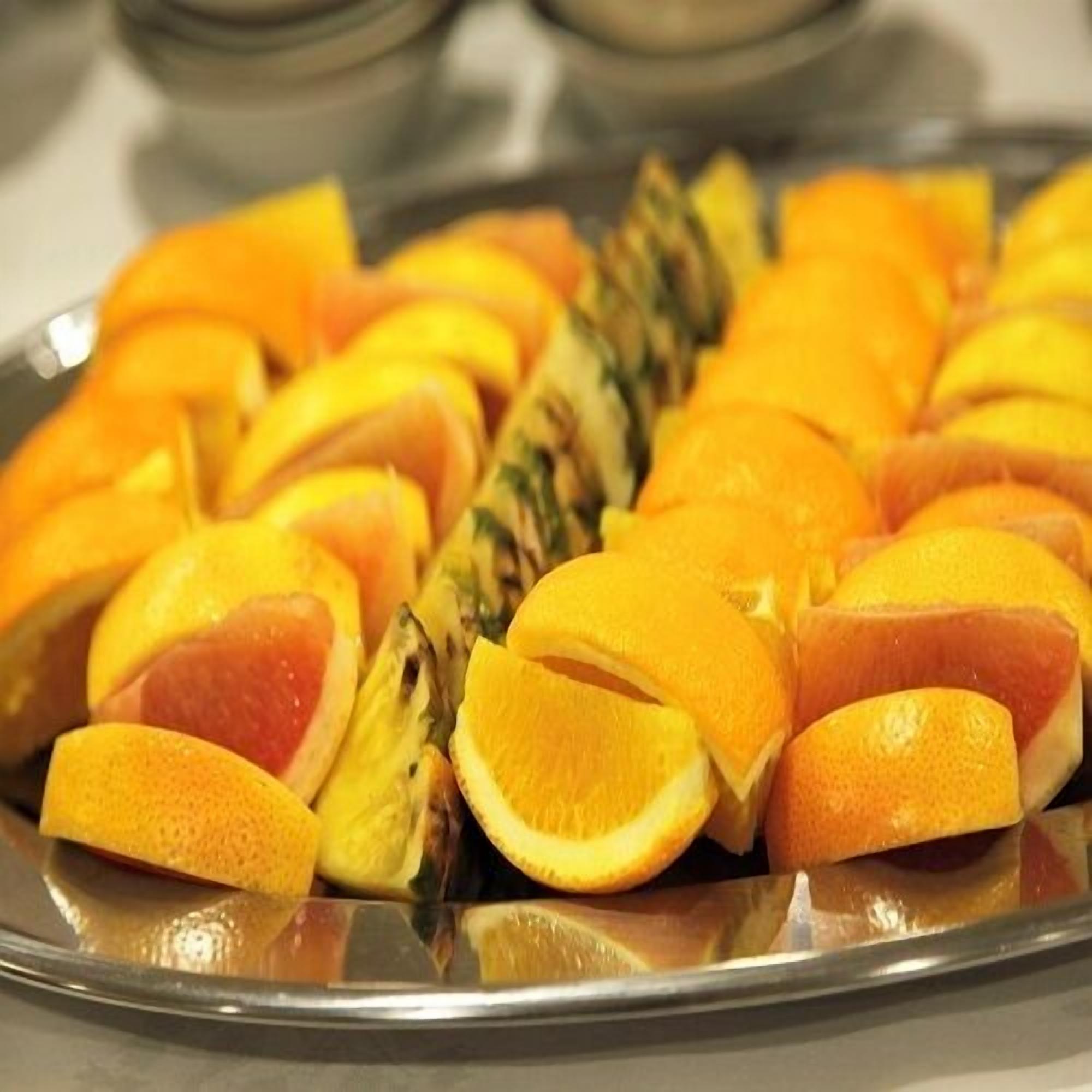Una bandeja con frutas cortadas, incluyendo naranjas y una piña.