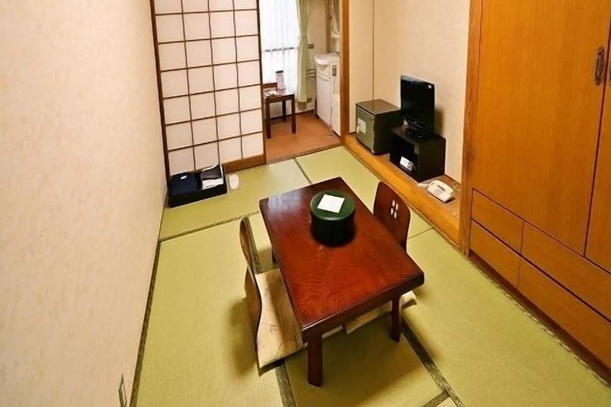 Une pièce de style japonais traditionnel, avec un sol recouvert de tatamis, une petite table sur laquelle repose un plateau noir, un téléviseur et une armoire en bois.