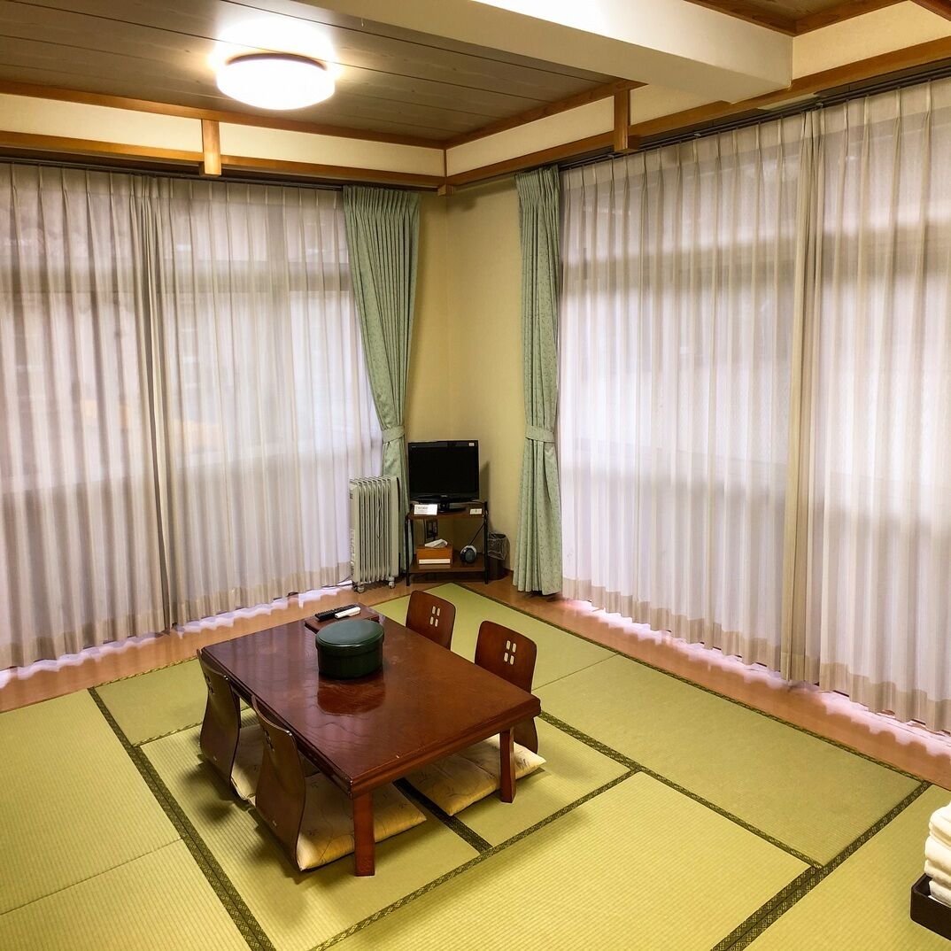 A traditional Japanese room with tatami flooring, a wooden table, and a television on a stand.