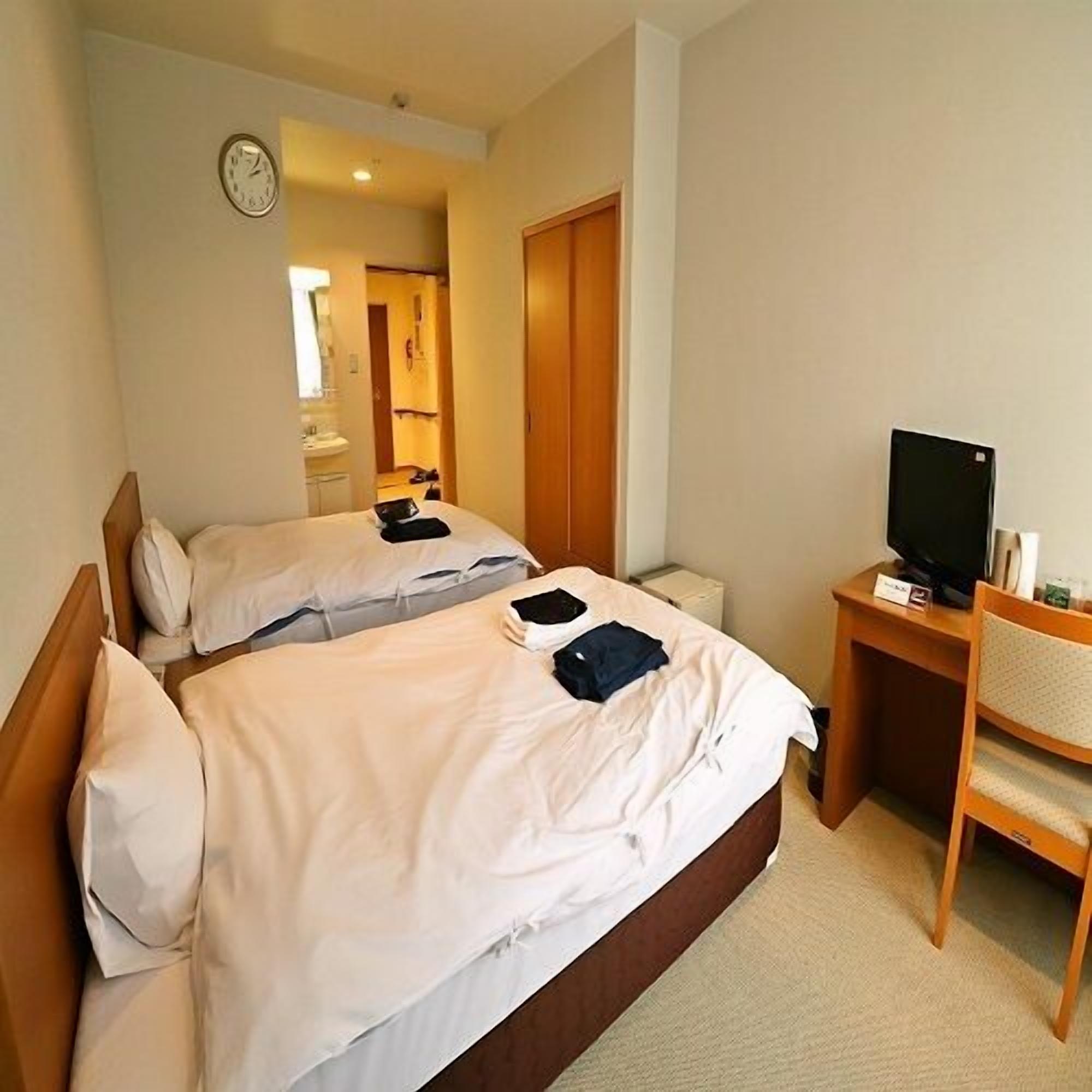 A hotel room with two beds, a desk with a television, and a clock on the wall.
