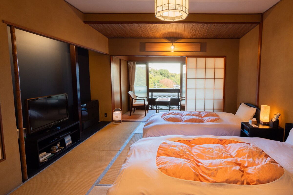 A hotel room with two beds, a TV, a desk, and a view of the outdoors.