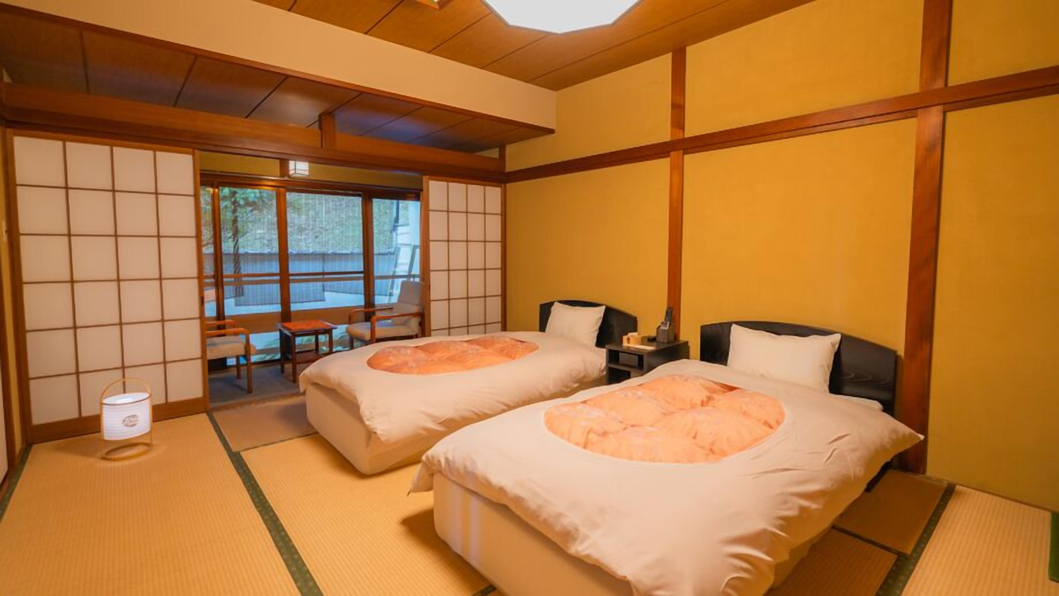 A traditional Japanese-style room with tatami flooring, two beds, a desk, and a view of a garden.