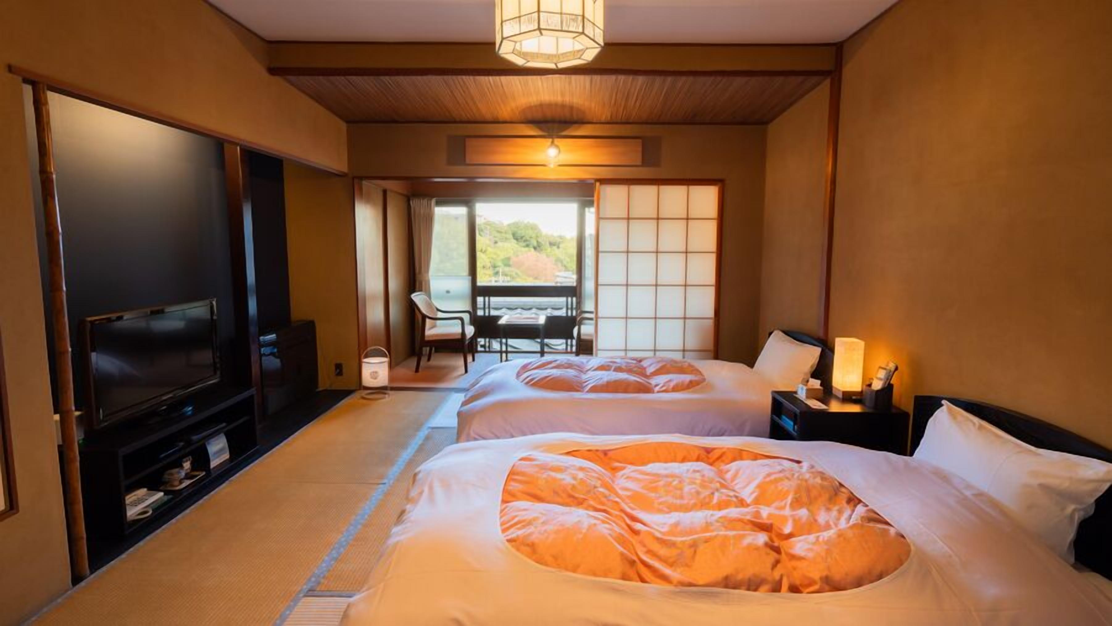 A hotel room with two beds, a TV, a desk, and a view of the outdoors.