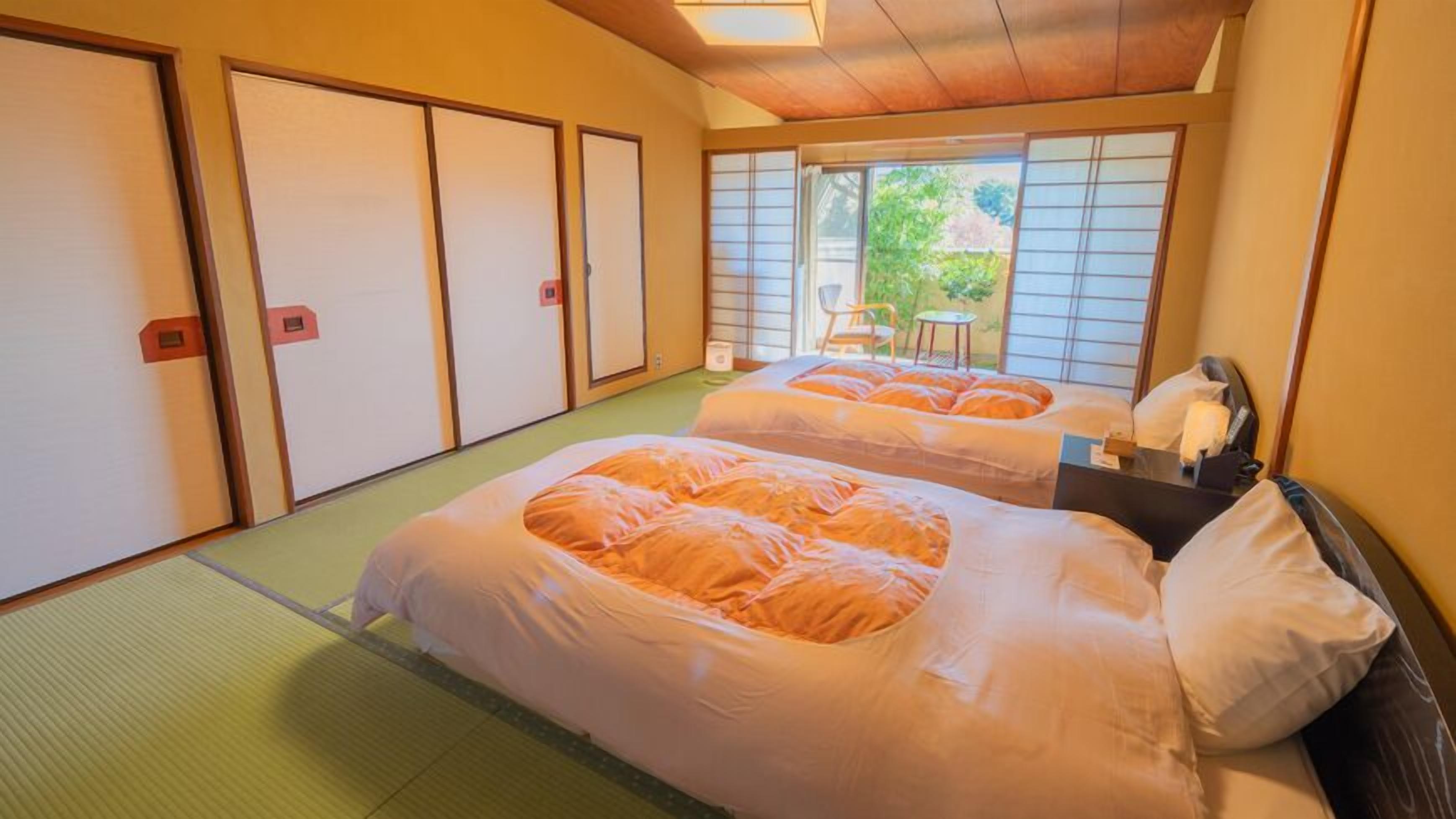 A traditional Japanese-style room with tatami flooring, two beds with orange bedding, a small table, and sliding doors.