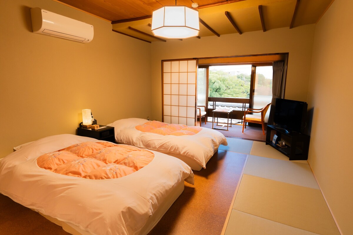 A hotel room with two beds, a TV, a desk, and a view of the outdoors.