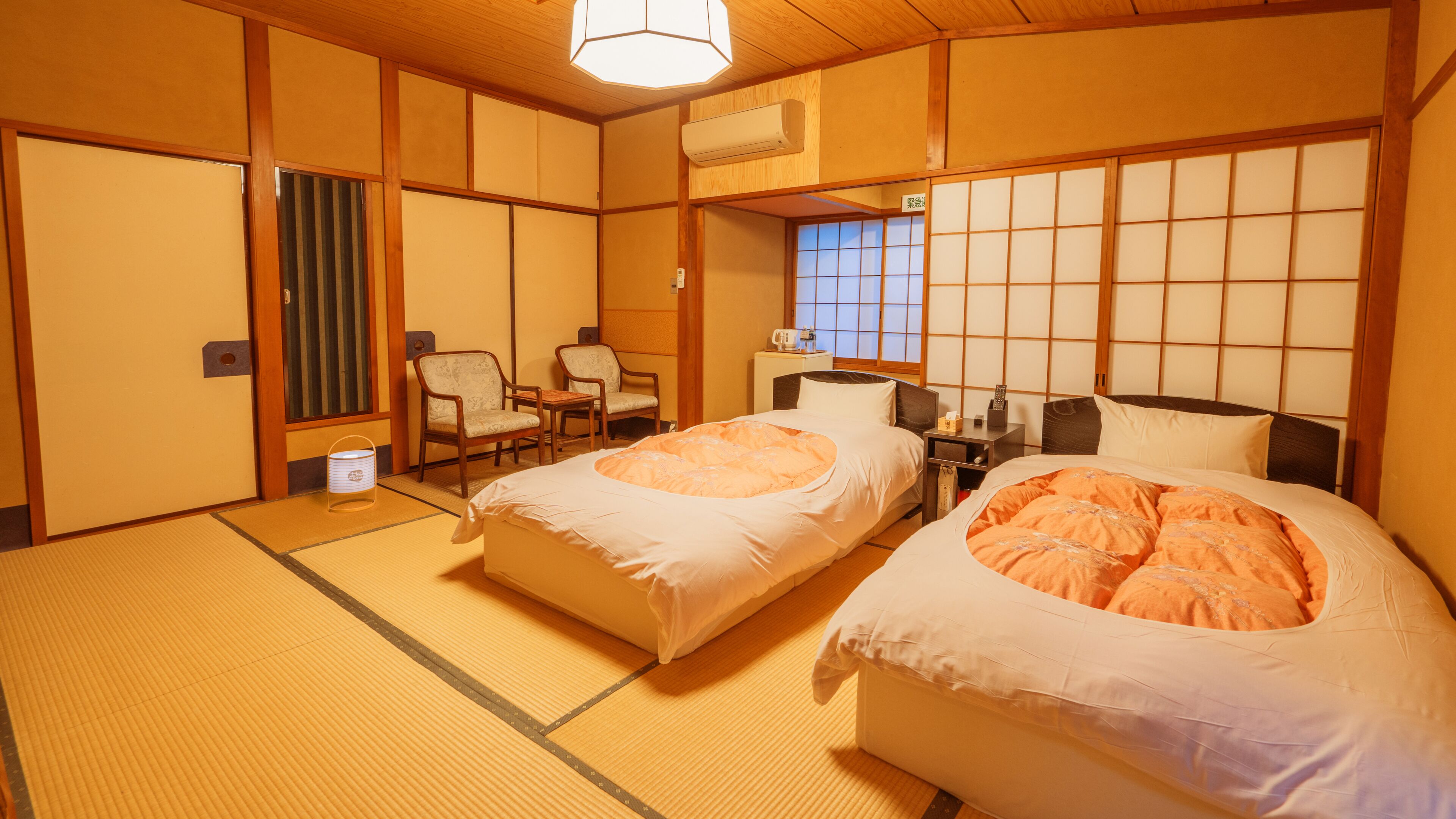 A traditional Japanese-style room with tatami flooring, two beds with white bedding, a wooden ceiling, and a shoji screen door.