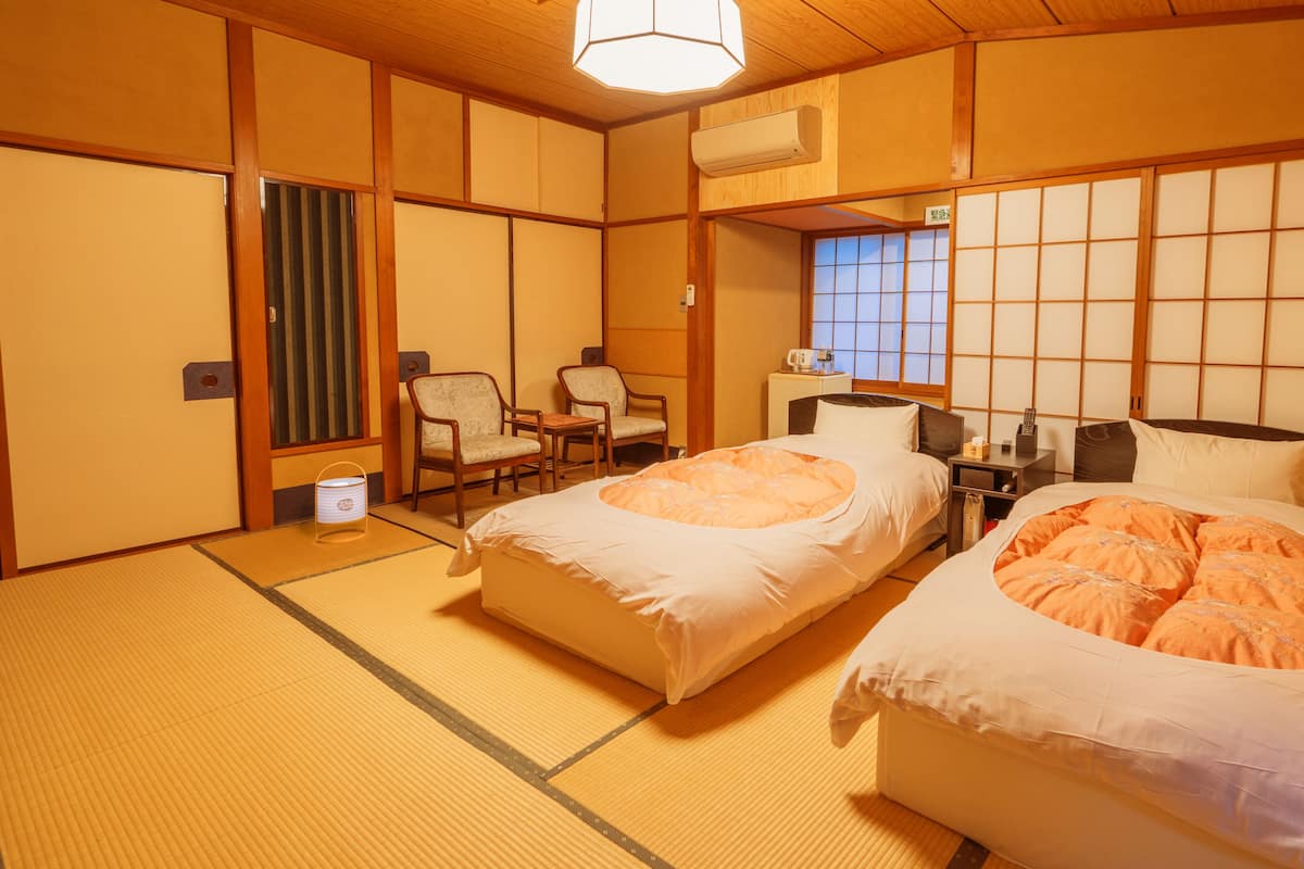 A traditional Japanese-style room with tatami flooring, two beds with white bedding, a wooden ceiling, and a shoji screen door.