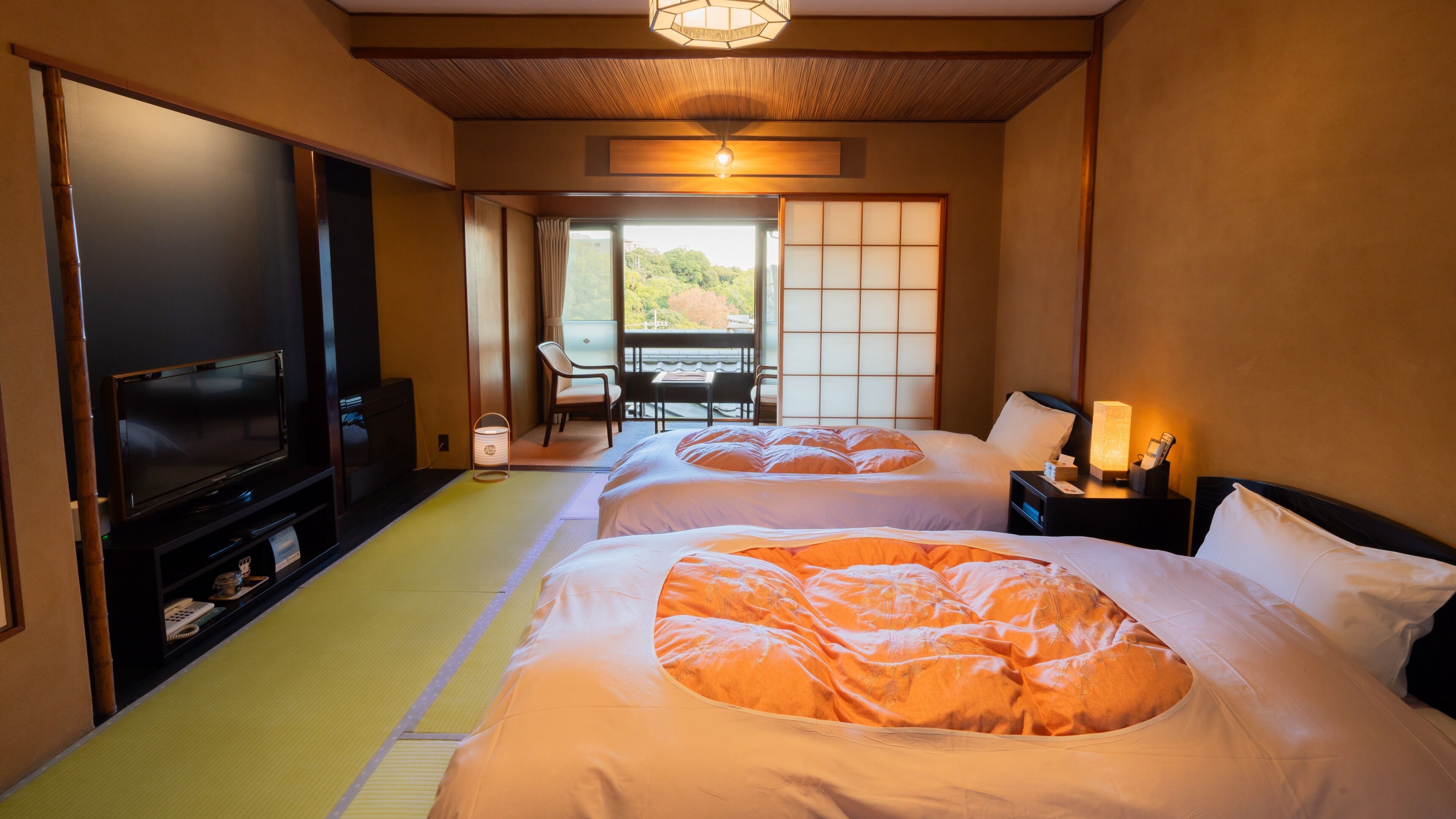 A hotel room with two beds, a TV, a desk, and a view of greenery outside.