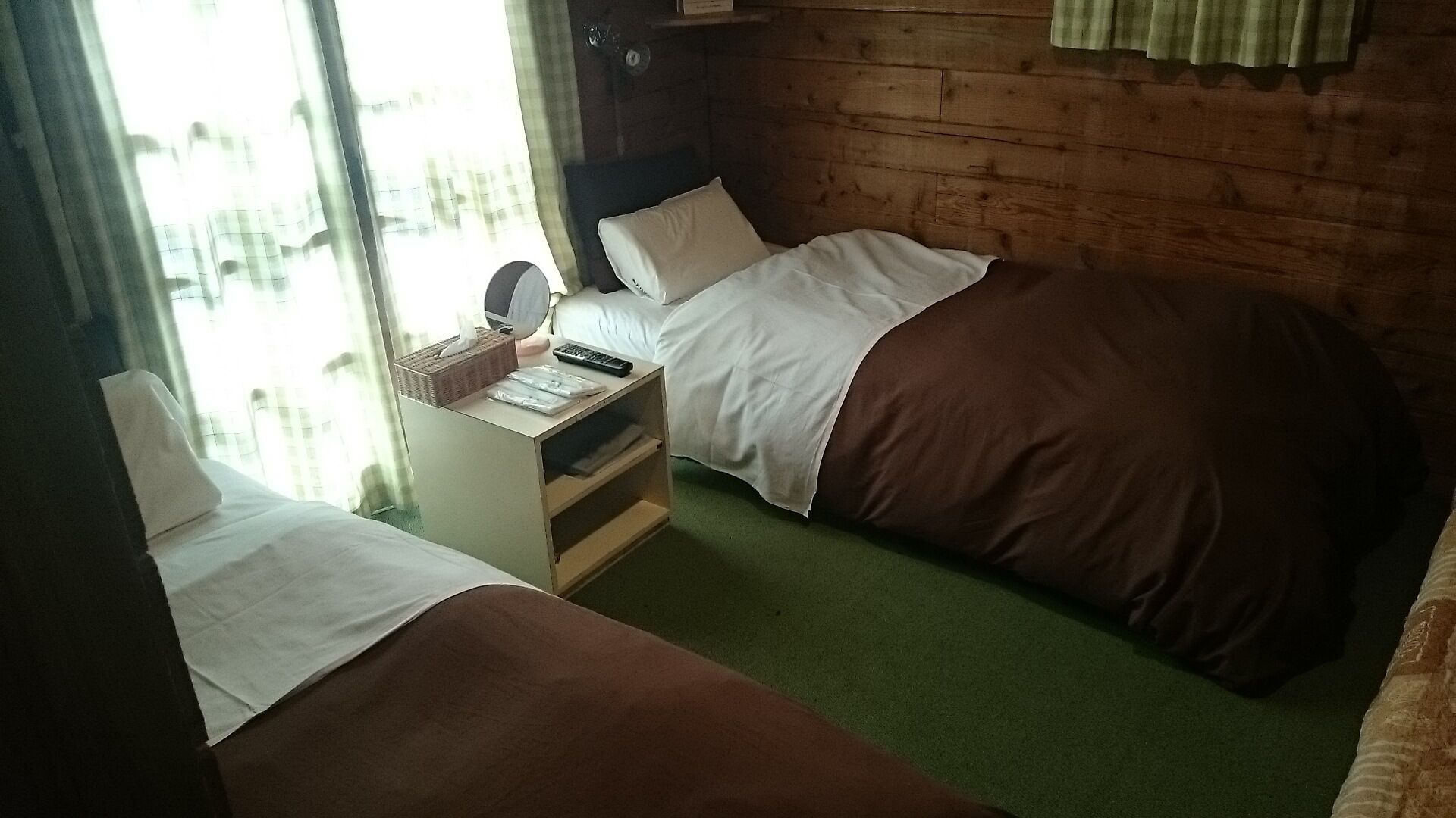 Une chambre avec deux lits, une table de chevet, un miroir et une fenêtre avec des rideaux.