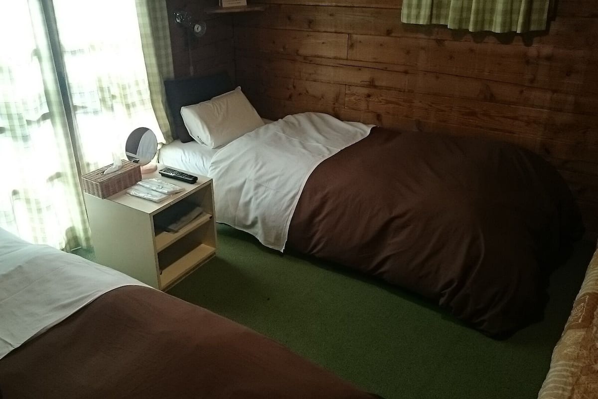 Une chambre avec deux lits, une table de chevet, un miroir et une fenêtre avec des rideaux.