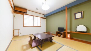 Una stanza tradizionale giapponese con pavimento in tatami, un tavolino, un televisore e un quadro appeso al muro.