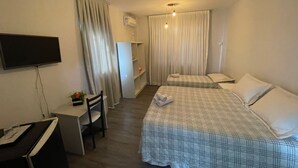 Et hotelværelse med to senge, et skrivebord, en stol, et fjernsyn og et vindue med gardiner.