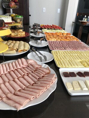 En buffet med forskellige serveringer, herunder kød, oste og frugt.