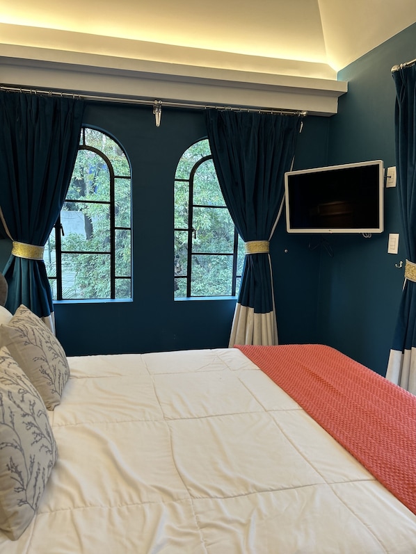 Un dormitorio con una cama grande, dos ventanas con cortinas, un televisor de pantalla plana y vista a zonas verdes.