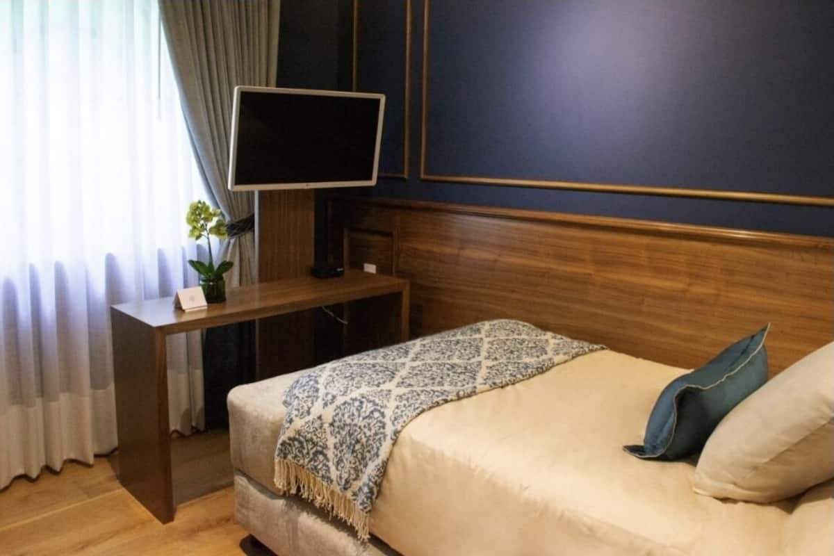 Una habitación de hotel con cama, escritorio y televisión, y ventana con cortinas.