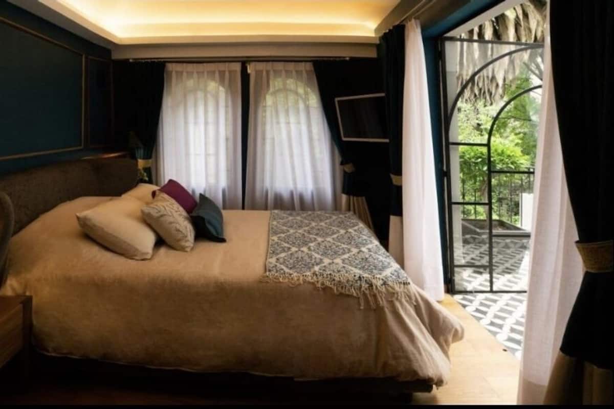 Un dormitorio con cama, mesita de noche, lámpara y cortinas.