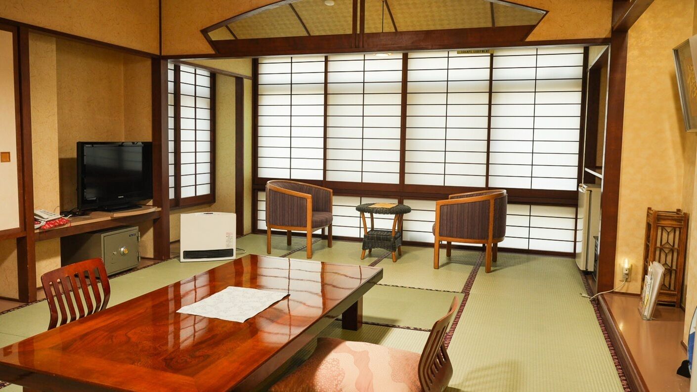 A traditional Japanese room with tatami flooring, a wooden table, chairs, a television, and sliding doors.