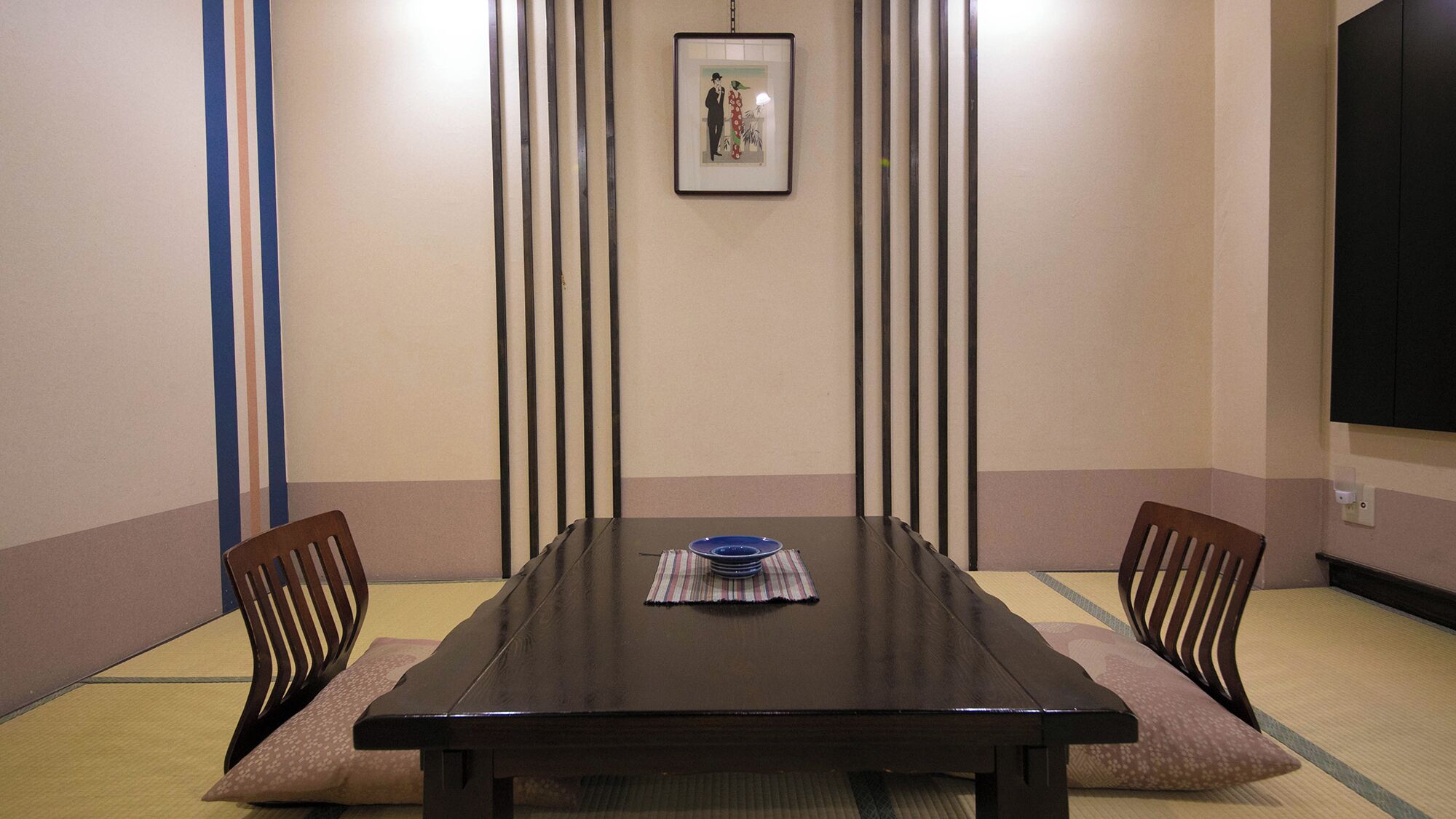 A conference room with a dark wooden table, two chairs, a framed picture on the wall, and a television mounted on the wall.