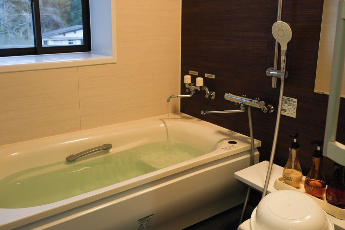 A bathroom with a bathtub, a window, a shower, and toiletries.