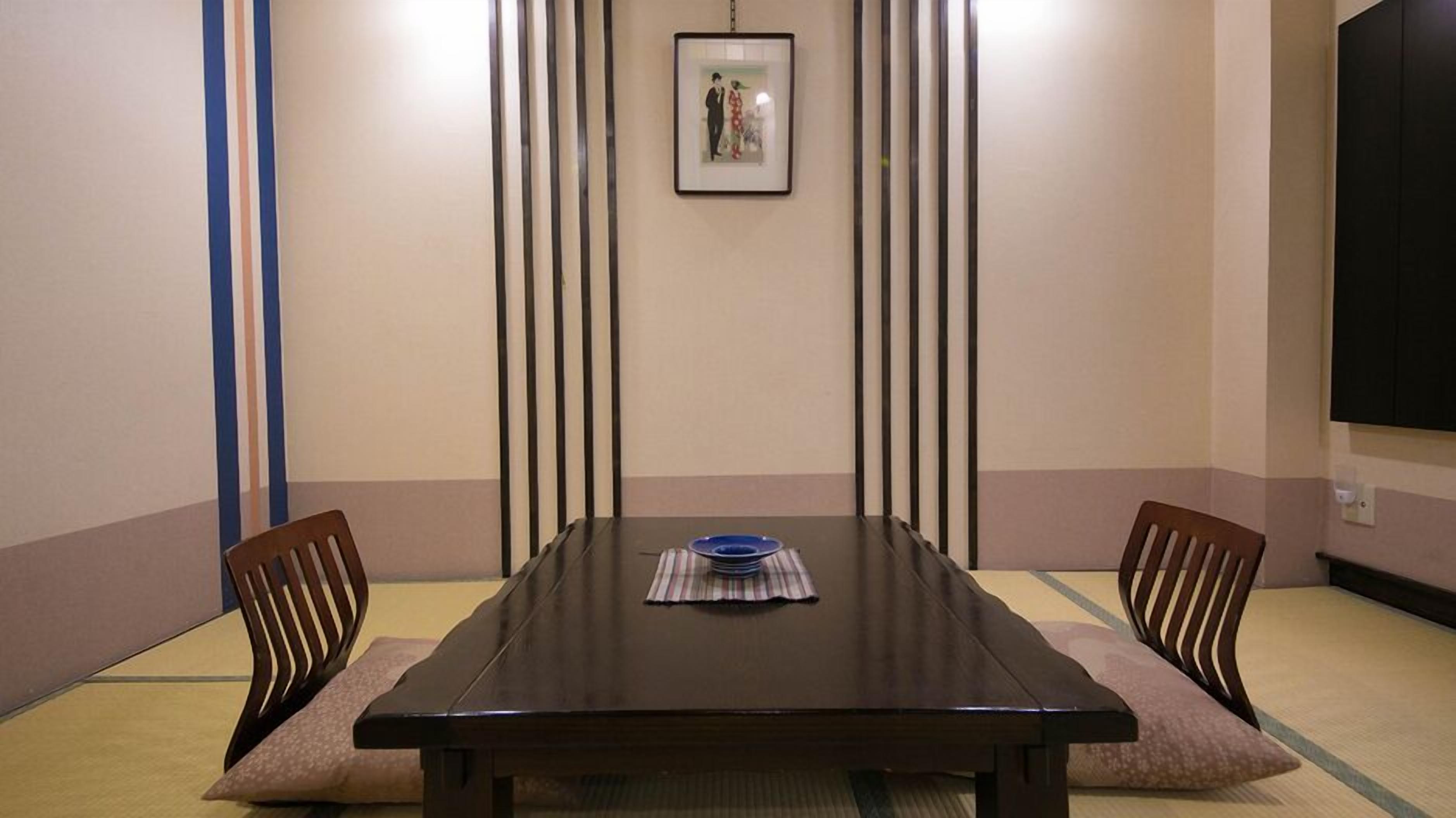 A conference room with a dark wooden table, two chairs, a framed picture on the wall, and a television mounted on the wall.
