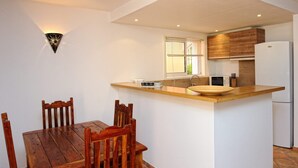 A compact kitchen with a wooden dining table and chairs, a built-in island with a sink, wooden cabinets, and a refrigerator. - Charming *** villa with heated pool, near downtown (porto vecchio)