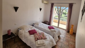 A bedroom with two beds, a window with curtains, an air conditioner, and a small table with a lamp. - Charming *** villa with heated pool, near downtown (porto vecchio)