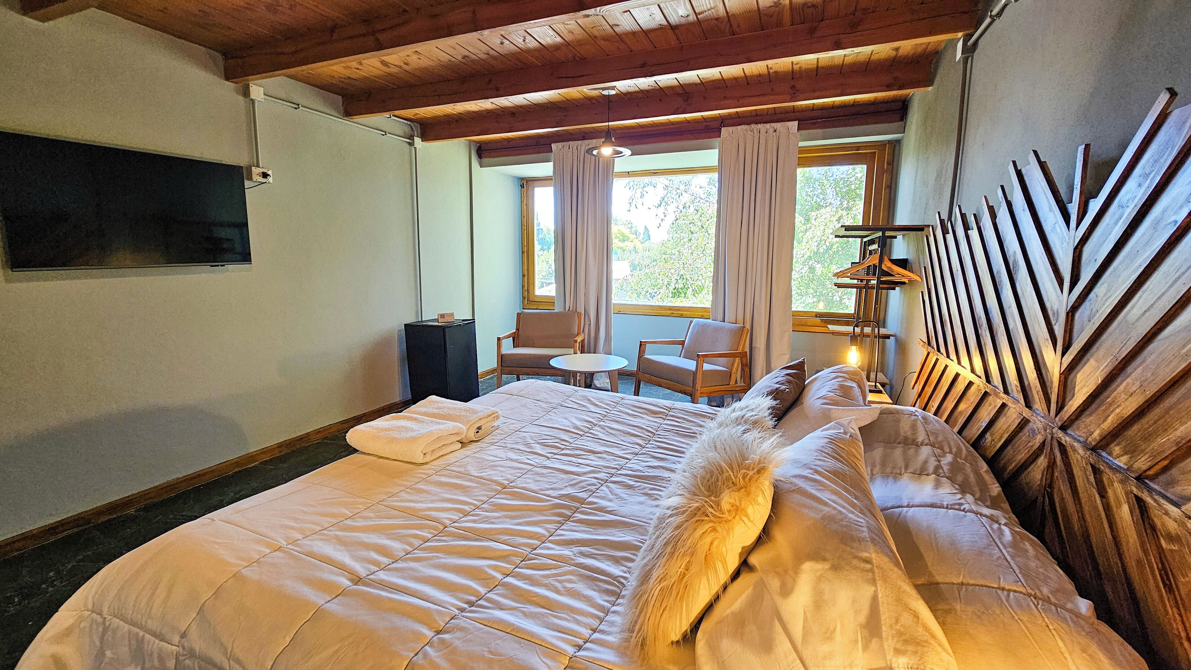 A bedroom with a large bed, two chairs, a small table, and a wooden headboard.